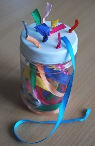 a glass jar filled with colorful streamers on top of a wooden table next to a blue ribbon