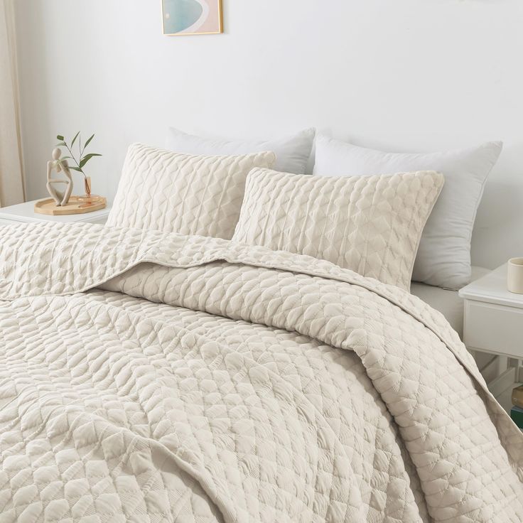 a bed with white comforter and pillows in a room next to a painting on the wall