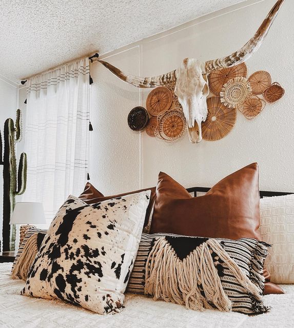 a bed topped with lots of pillows next to a wall mounted cow skull on the wall