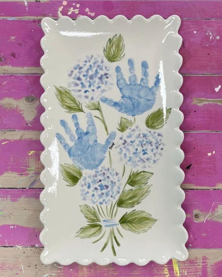 a white plate with blue flowers painted on it and two hands in the shape of handprints