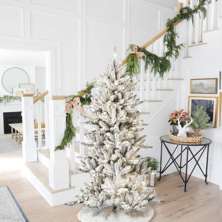 a white christmas tree in the middle of a room with stairs and pictures on the wall