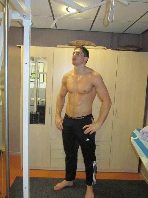 a man with no shirt standing in front of a mirror wearing black sweatpants and shorts