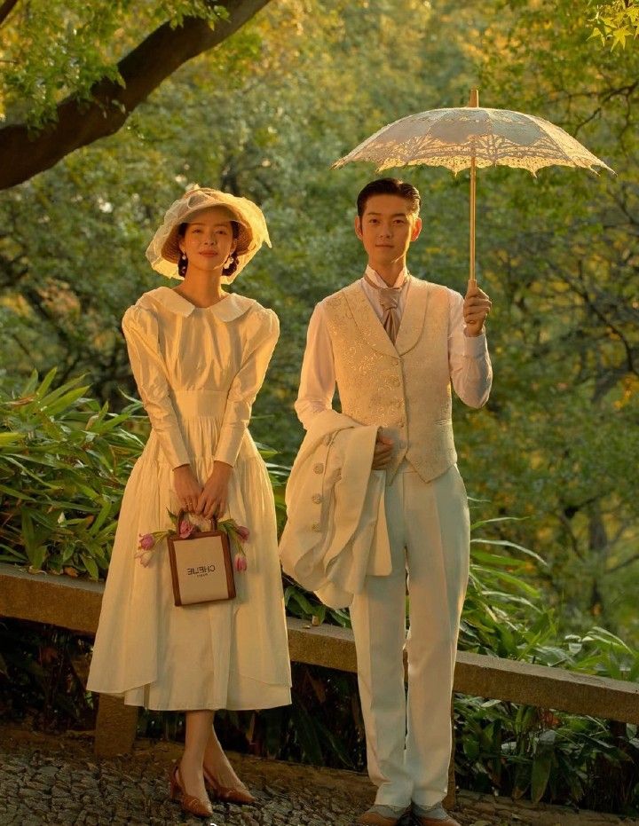 a man and woman dressed in white holding an umbrella while standing next to each other