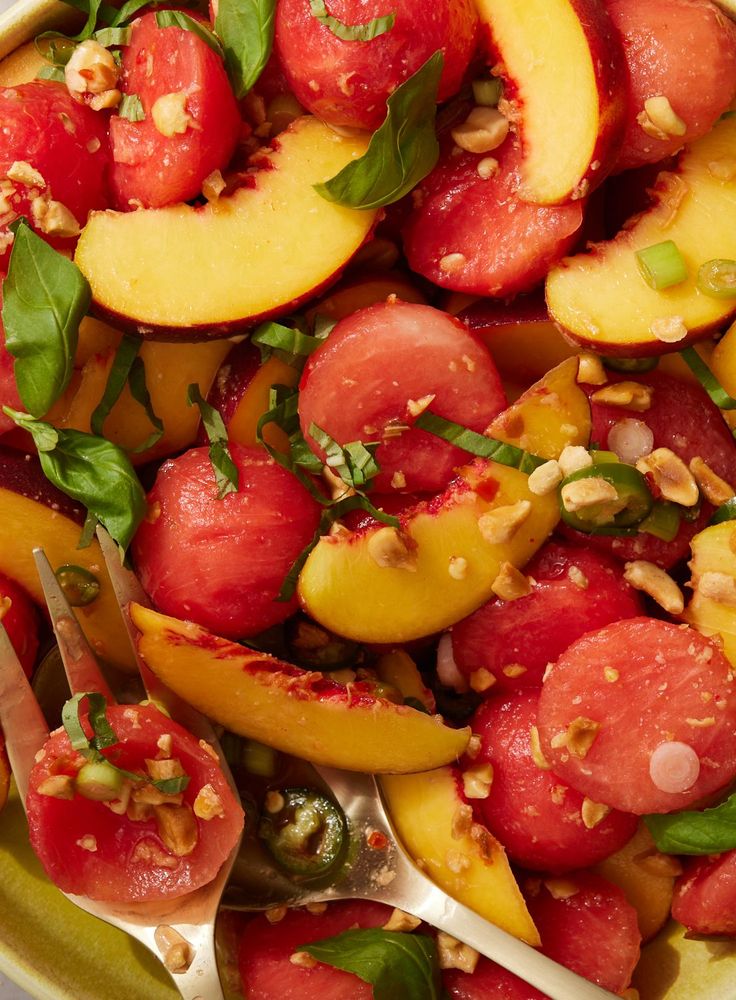 a bowl filled with sliced peaches and green leaves next to a spoon on top of a table