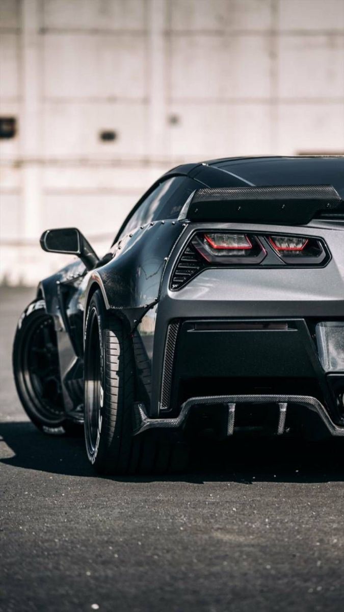 the rear end of a black sports car parked in a parking lot next to a building