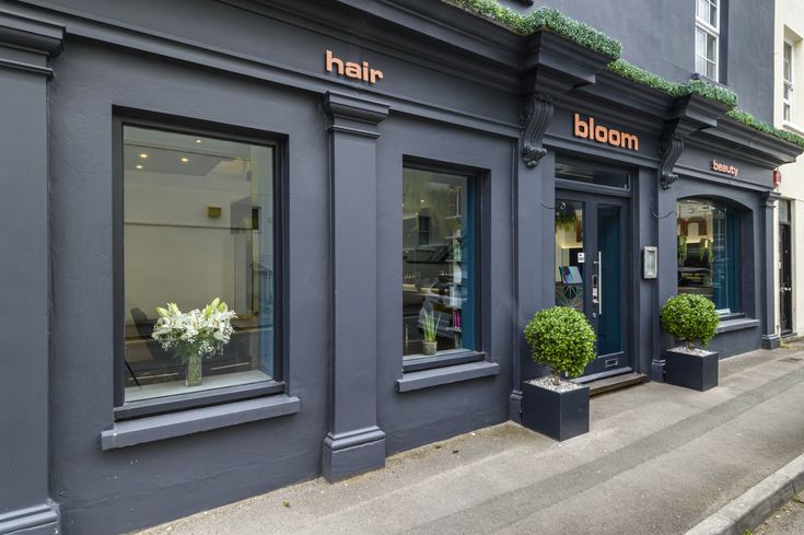 the front of a hair salon with large windows and planters on the side of the building