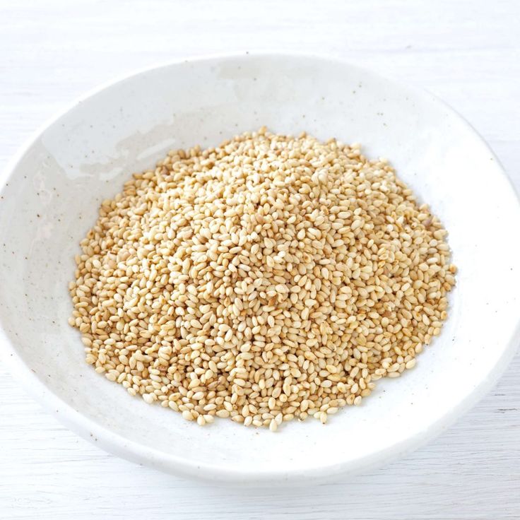 a white bowl filled with sesame seeds on top of a wooden table