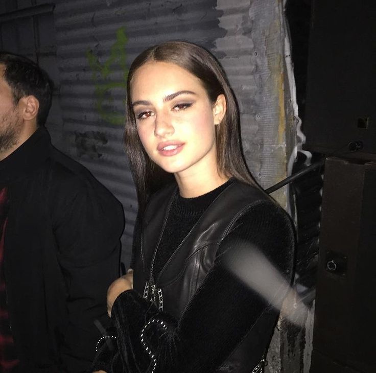 a woman standing next to a man in a black shirt and leather jacket at night