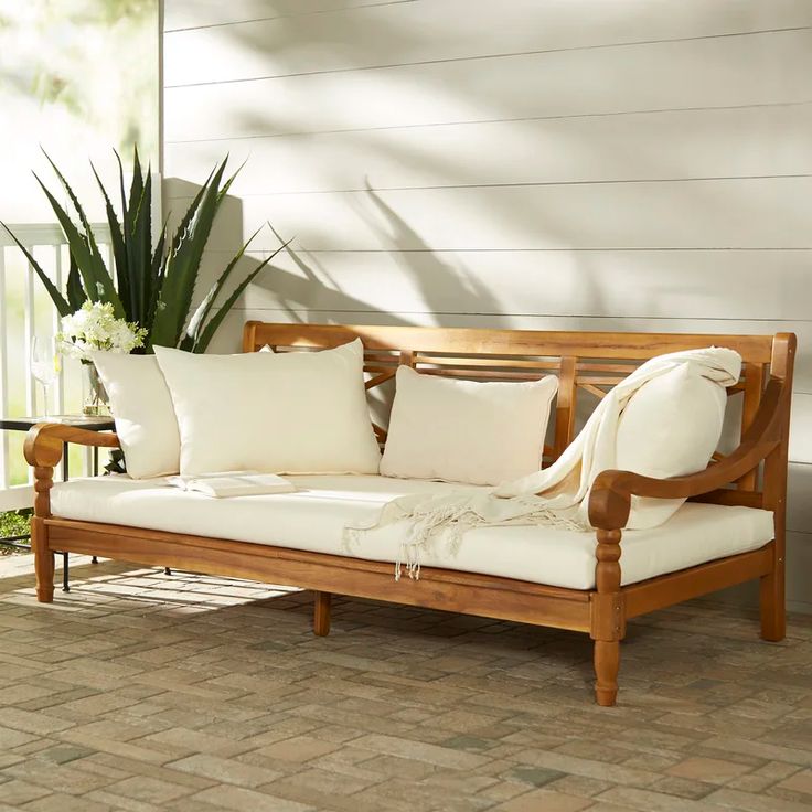 a wooden couch sitting on top of a brick floor next to a potted plant