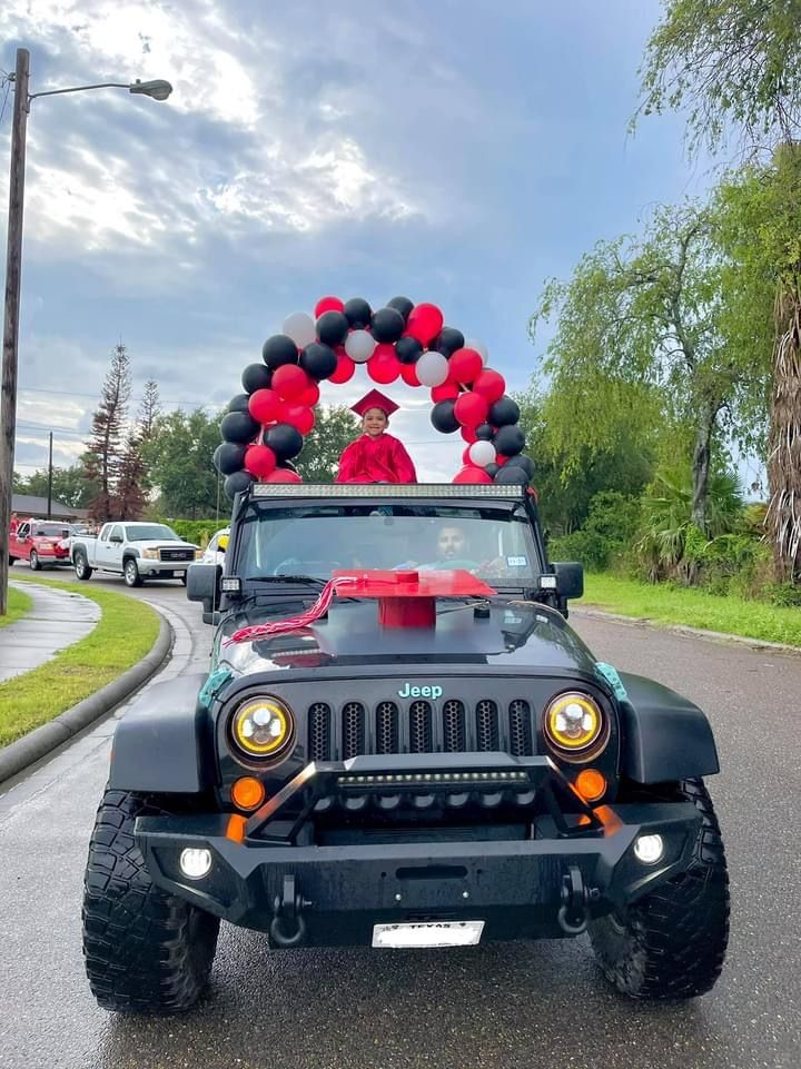 a jeep decorated with black and red balloons is driving down the street in front of a man