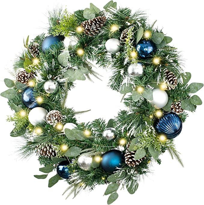 a christmas wreath with blue and white ornaments on it, surrounded by greenery and pine cones