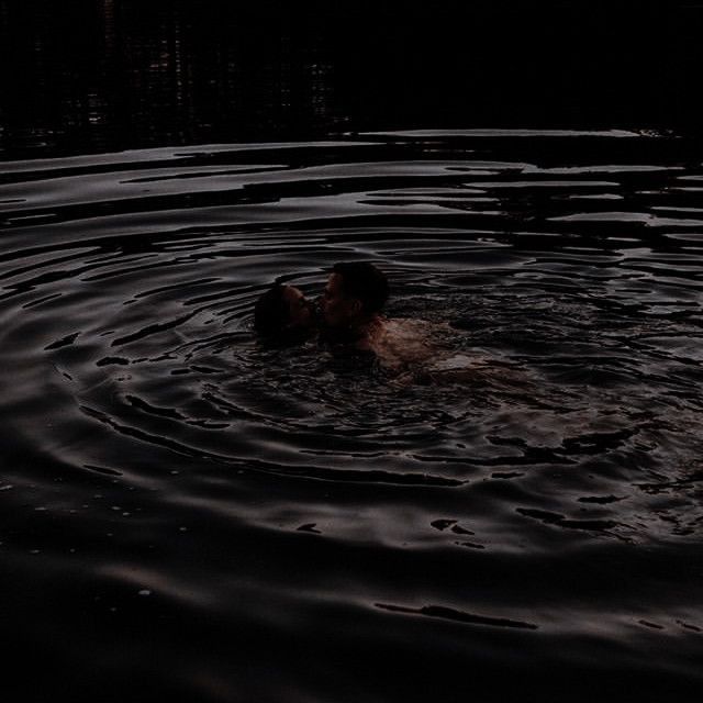 two people are swimming in the water at night, one is kissing the other's head