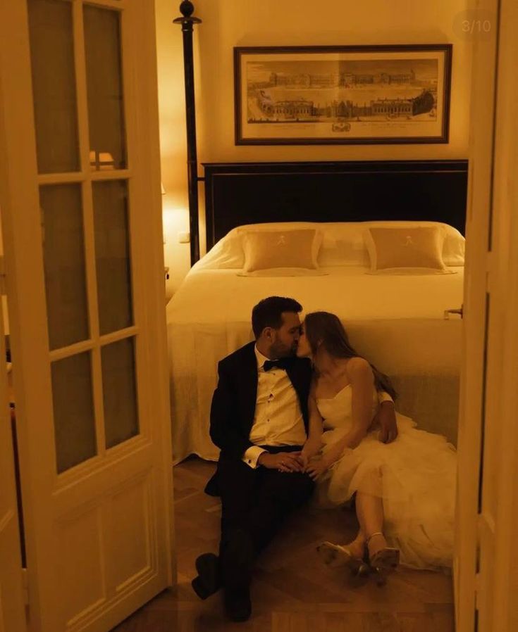 a man and woman sitting on the floor in front of a bed