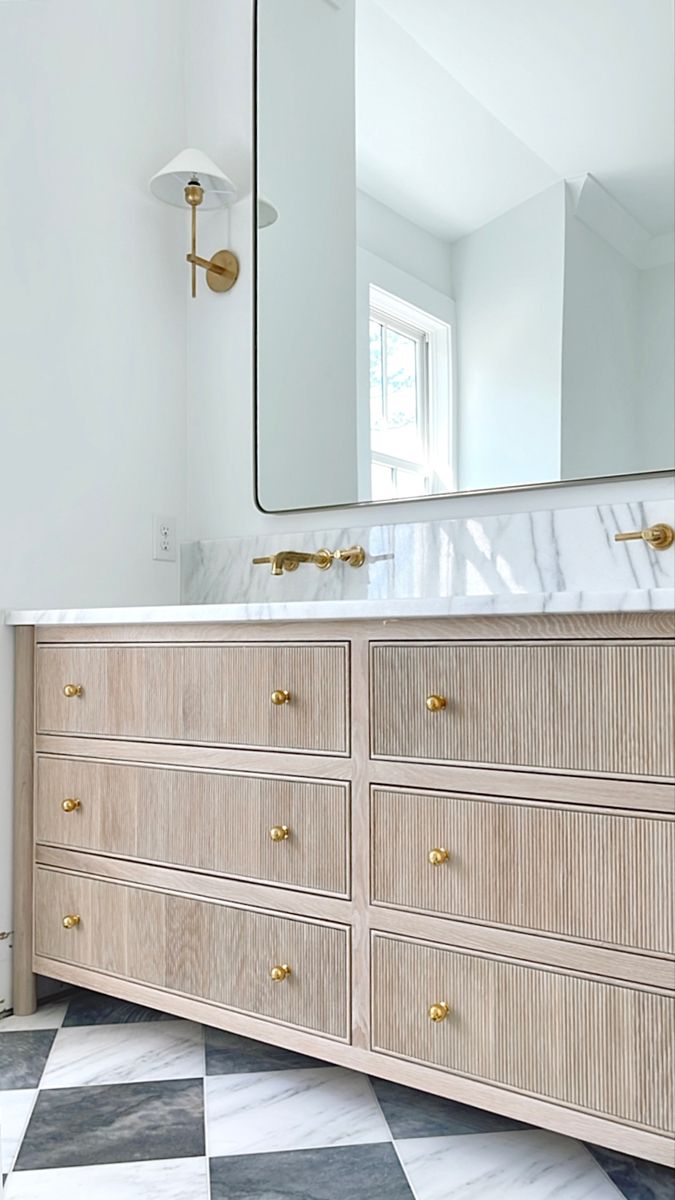 a bathroom vanity with marble counter top and gold handles on the drawers, along with a large mirror above it