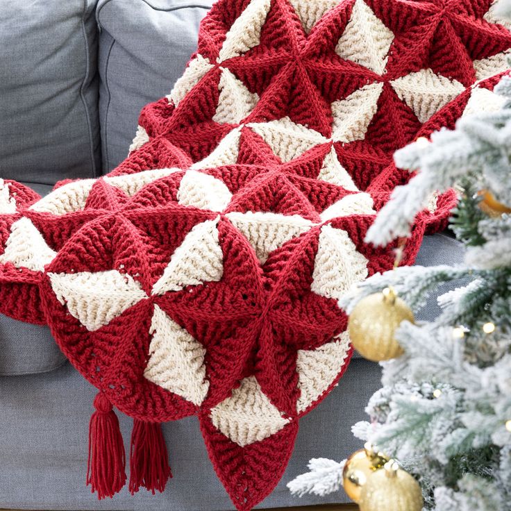 a red and white crocheted blanket sitting on top of a couch next to a christmas tree