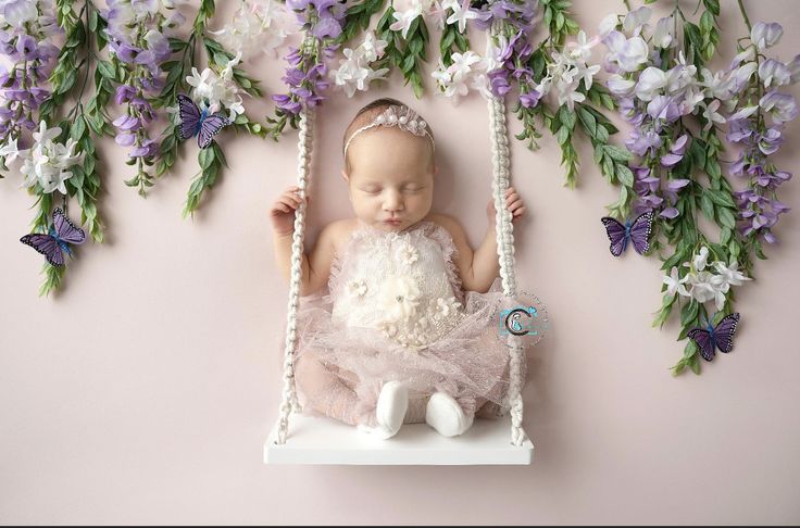 a baby in a pink dress is sitting on a swing surrounded by purple and white flowers