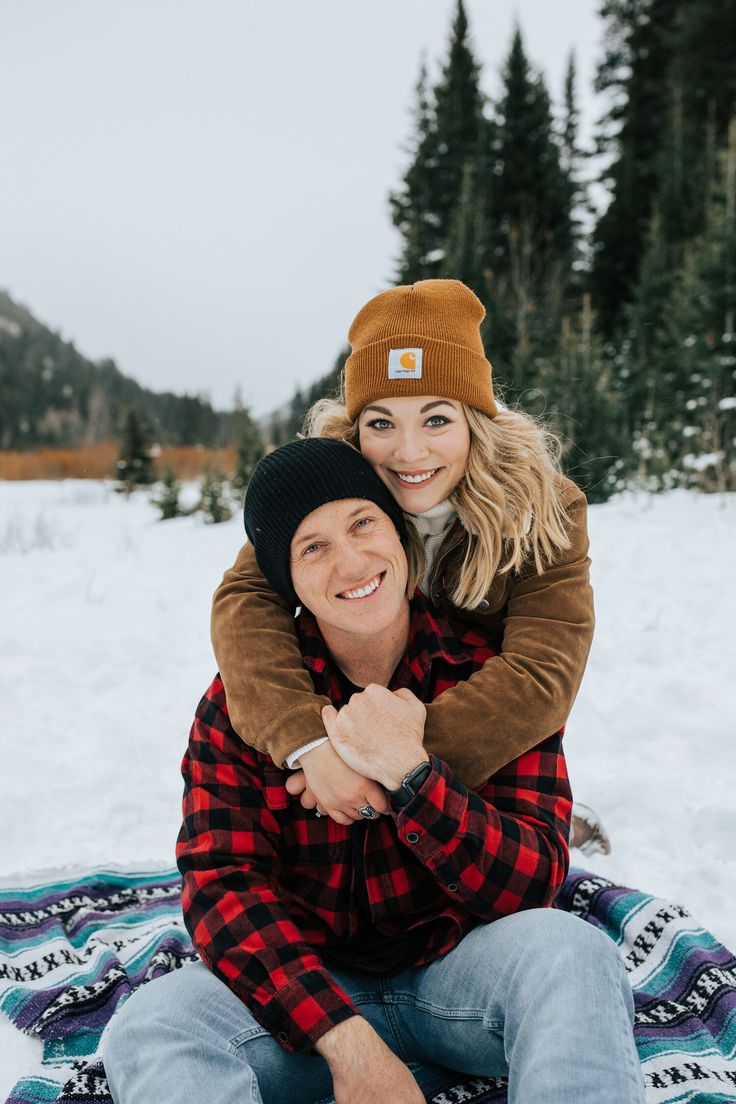 a man and woman are sitting on a blanket in the snow, smiling at the camera