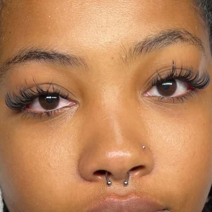 a close up of a woman's nose with fake eyelashes and piercing on her nose