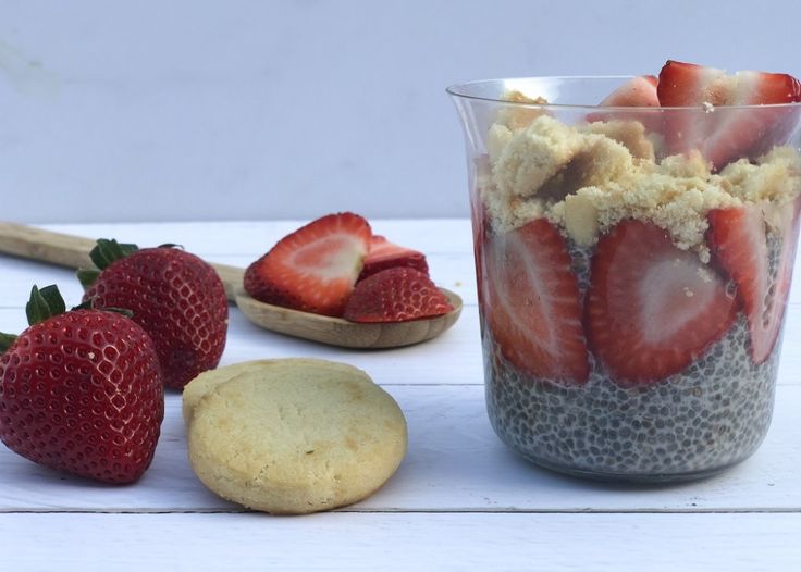 some strawberries and cookies are in a glass on a white table with two spoons