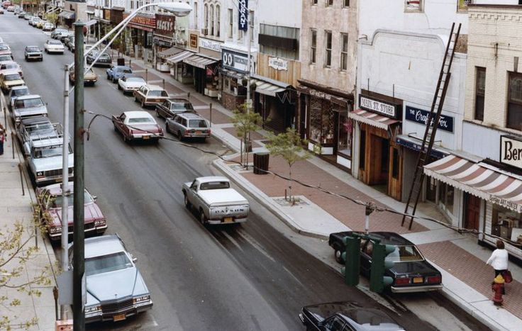 a city street filled with lots of traffic next to tall buildings and parked cars on the side of the road