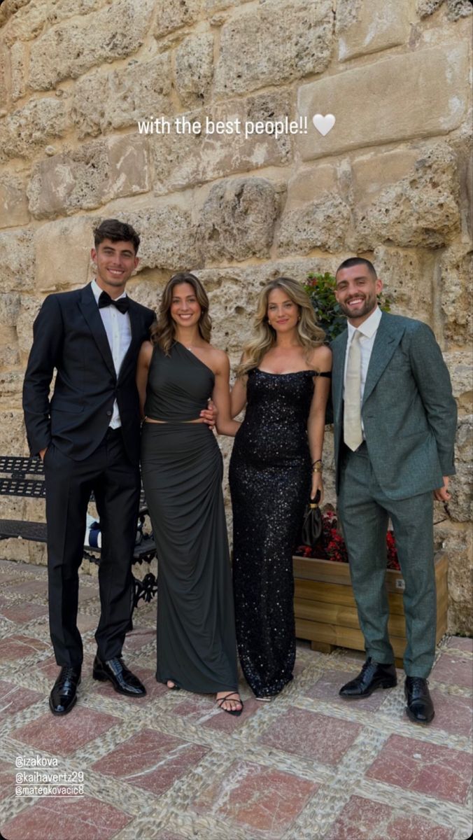 three people in formal wear standing next to each other near a stone wall and bench