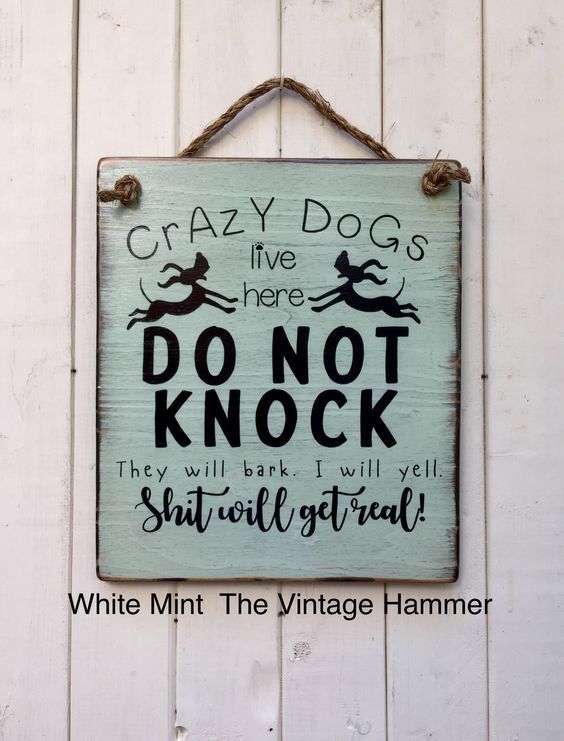 a sign hanging on the side of a white wooden wall that says, crazy dogs live here don't knock they will bark i will tell you shall steal it