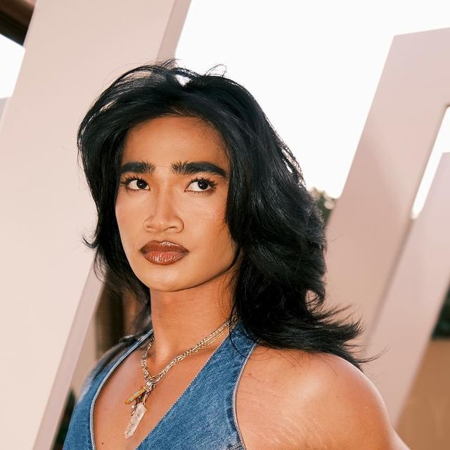 a close up of a person wearing a blue shirt and necklace with long black hair