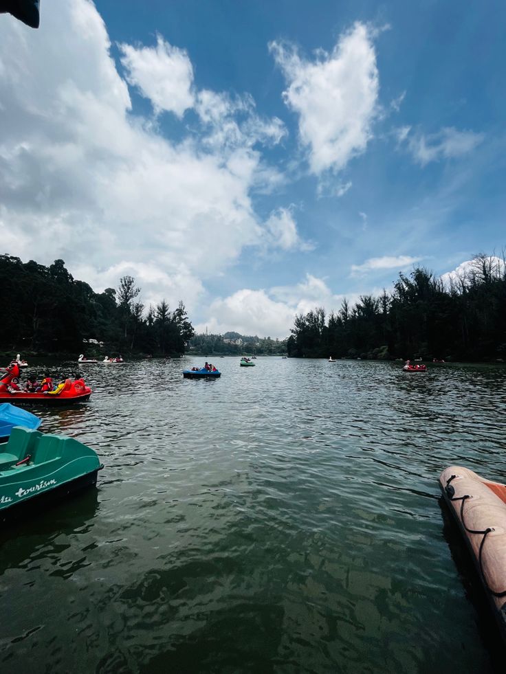 several boats floating on top of a lake under a cloudy blue sky with white clouds