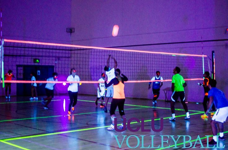 group of people playing volley ball on an indoor court with neon lights in the background