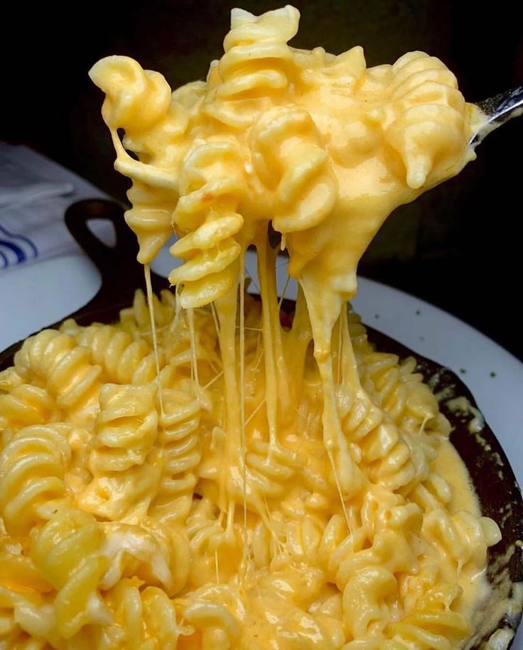 a spoon full of macaroni and cheese being held over the top of it