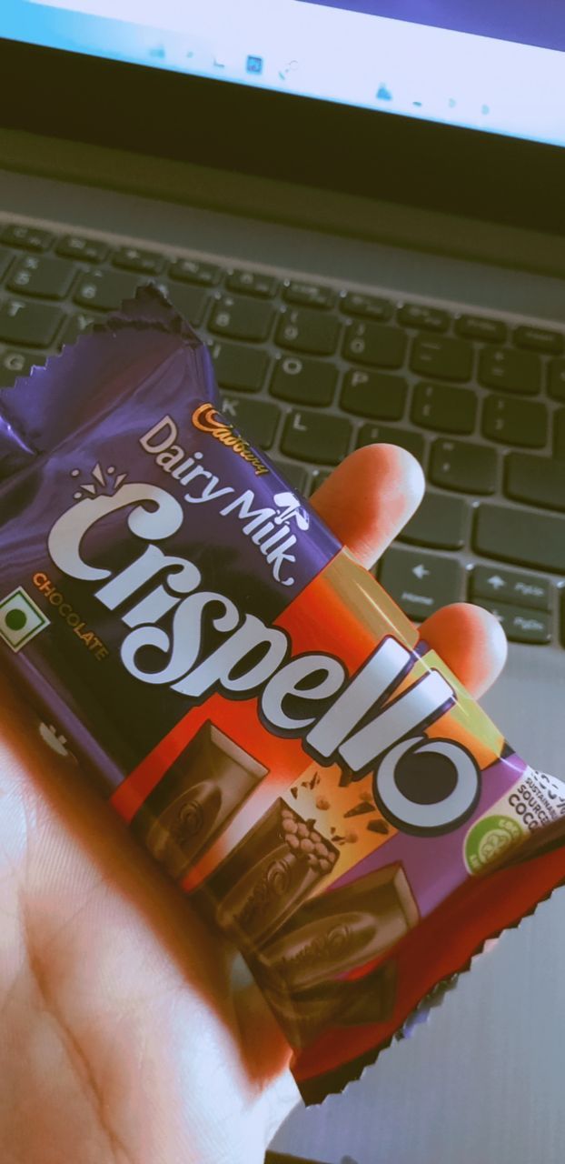 a person holding a bar of chocolate in front of a laptop