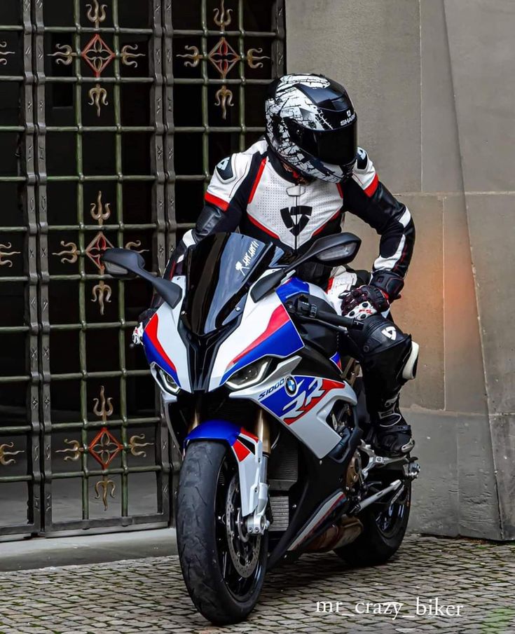 a man riding on the back of a motorcycle next to a metal gate in front of a building