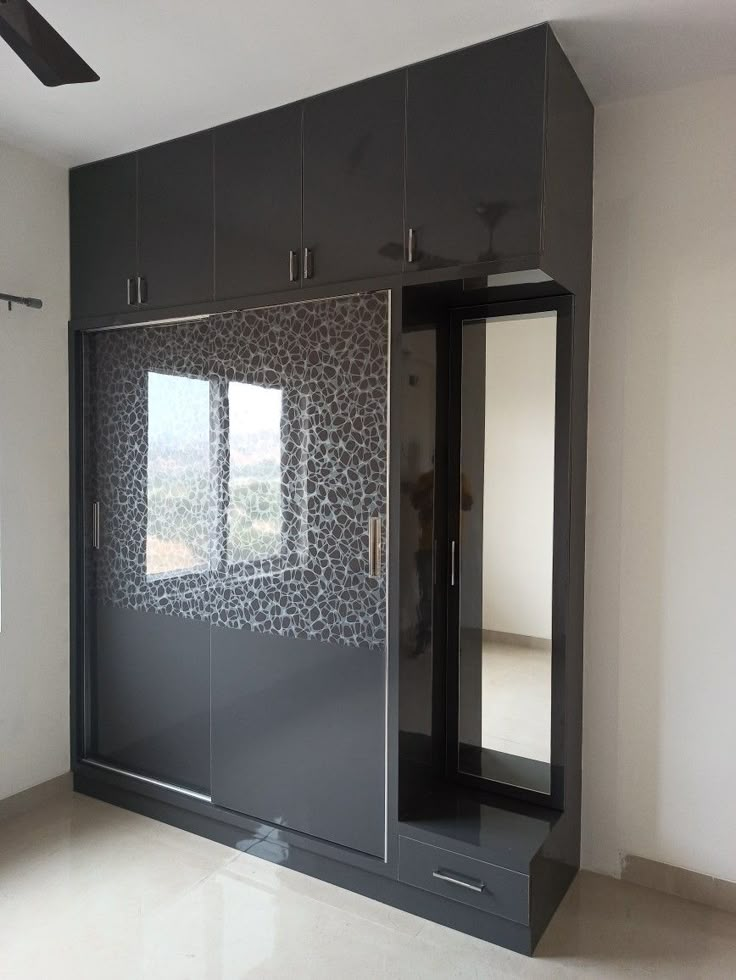 an empty room with black cabinets and mirrored glass doors on the wall, in front of a large window