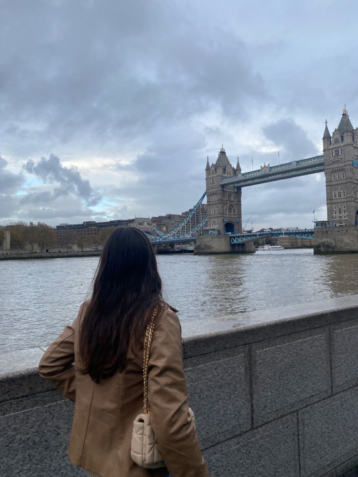 a woman is looking at the water and tower bridge in london, england on a cloudy day