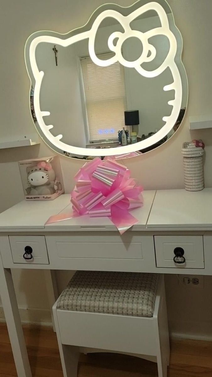 a white desk with a hello kitty lighted mirror on it's side and a pink bow in front of the mirror