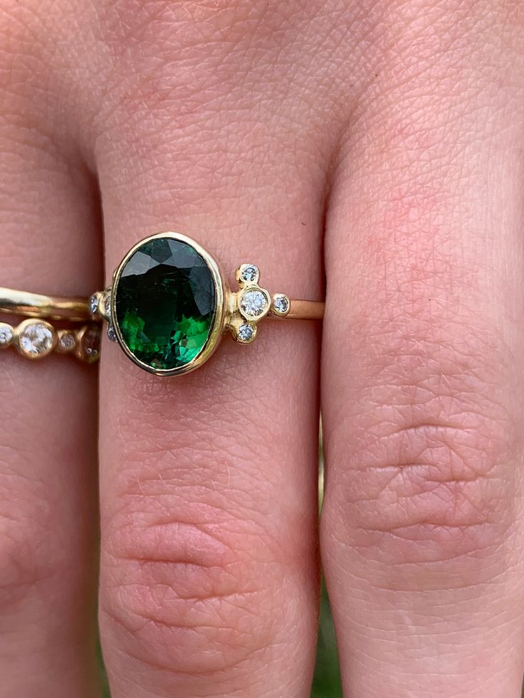 A perfect emerald green Tourmaline is set in Emily's 14k gold Trefoil cluster setting with a freeform band. We originally saw this as being a unique engagement ring but it would be just as wonderful as an everyday bit of sparkle and looks phenomenal with our halo bands Approximate stone size: 10mm x 8mm TCW tourmaline: 2.5ct TCW diamonds: .12ct Mohs Stone Hardness: 7.5-8 This one of a kind piece is handmade in Emily's Hudson Valley studio. If you have questions about sizing, shipping or need hel Emerald Cut Green Ring With Rose Cut Diamonds, Green Cluster Ring With Rose Cut Diamonds, Green Emerald Cluster Ring With Rose Cut Diamonds, Green Emerald Jewelry With Rose Cut Diamonds, Oval Green Rose Cut Diamond Rings, Heirloom Green Cluster Ring, Unique Oval Emerald Ring In 14k Gold, Emerald Cluster Ring With Gemstones, Oval Emerald Ring In 14k Gold