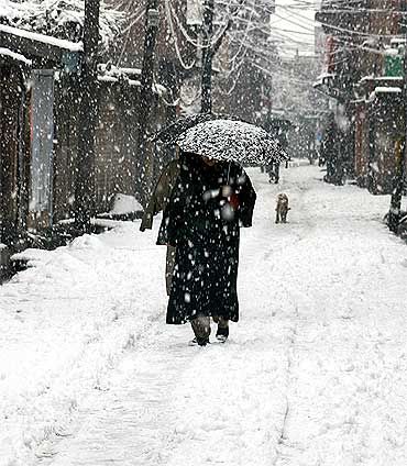 a woman walking down a snow covered street with an umbrella in the middle of it