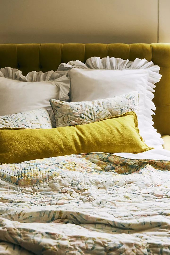 a bed with white and yellow pillows on it's headboard next to a window