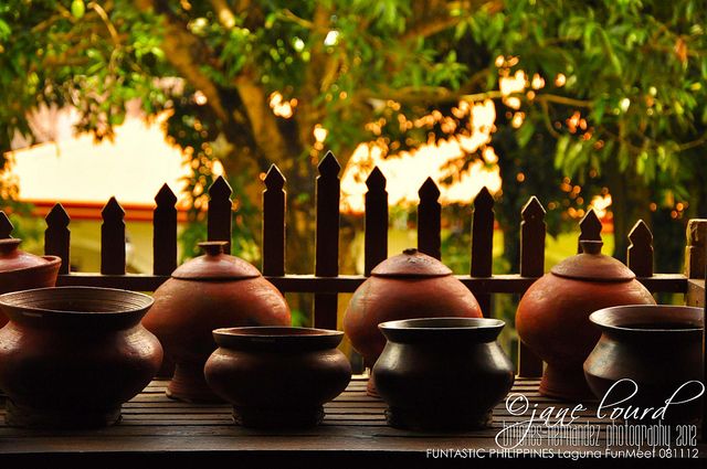 pots and bowls are lined up on a wooden table with a fence in the background