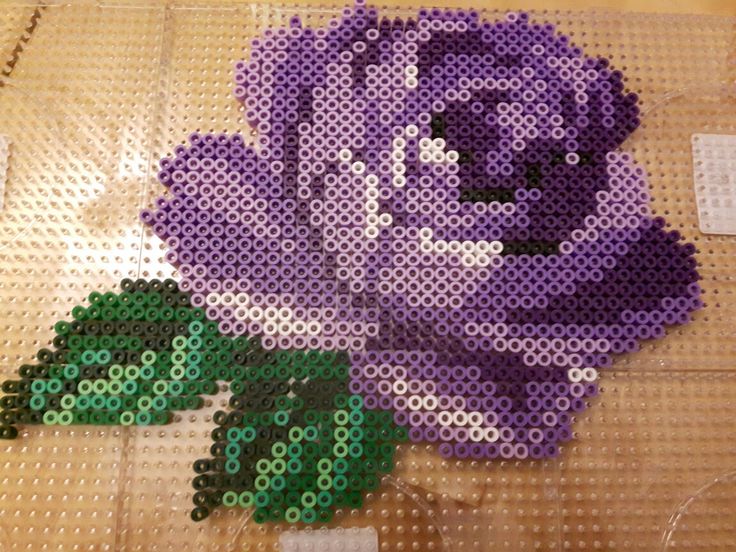 a purple flower made out of legos on top of a plastic sheet with green leaves