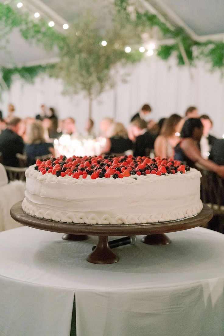 a white cake with berries on it sitting on top of a table in a banquet hall