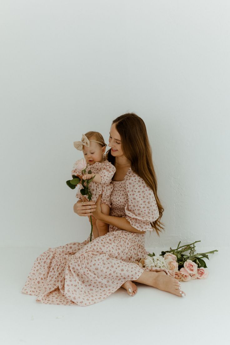 a woman holding a baby in her arms while sitting on the floor next to flowers