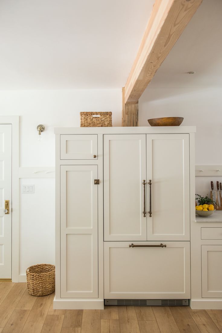 a white kitchen with wooden floors and cabinets in the corner, along with a basket on top of the cupboards