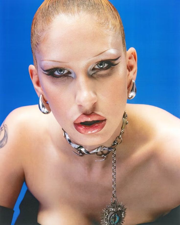 a woman with tattoos and piercings on her head is posing for the camera in front of a blue background