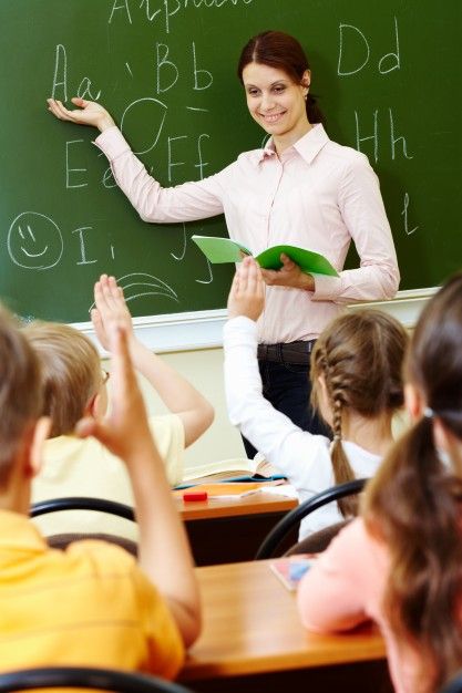 there is a woman teacher teaching in front of her class at the blackboard with two hands up