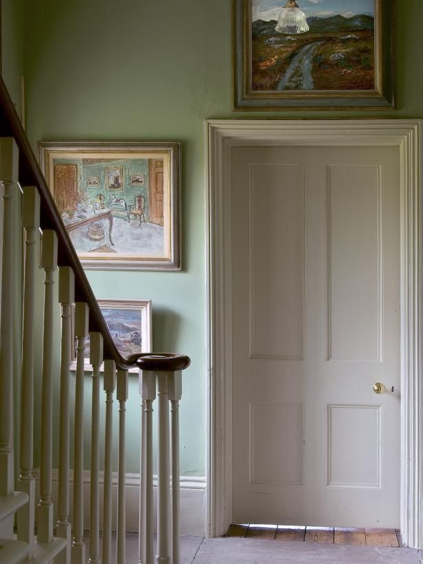 a hallway with green walls and paintings on the wall, along with white banisters