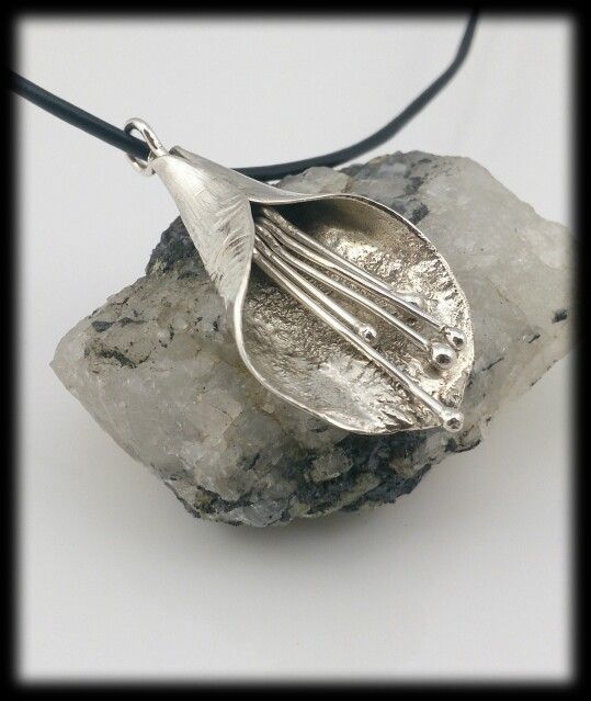 a silver leaf pendant sitting on top of a rock