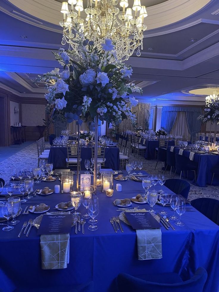 a table is set with blue linens and silver place settings for an elegant dinner