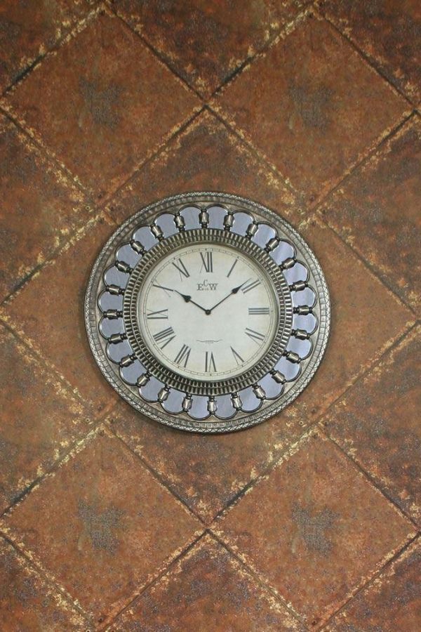 a clock sitting on the floor in front of a wall with brown and tan tiles