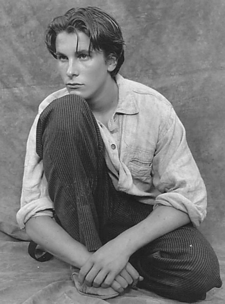 an old black and white photo of a young man sitting on the ground with his hands in his pockets